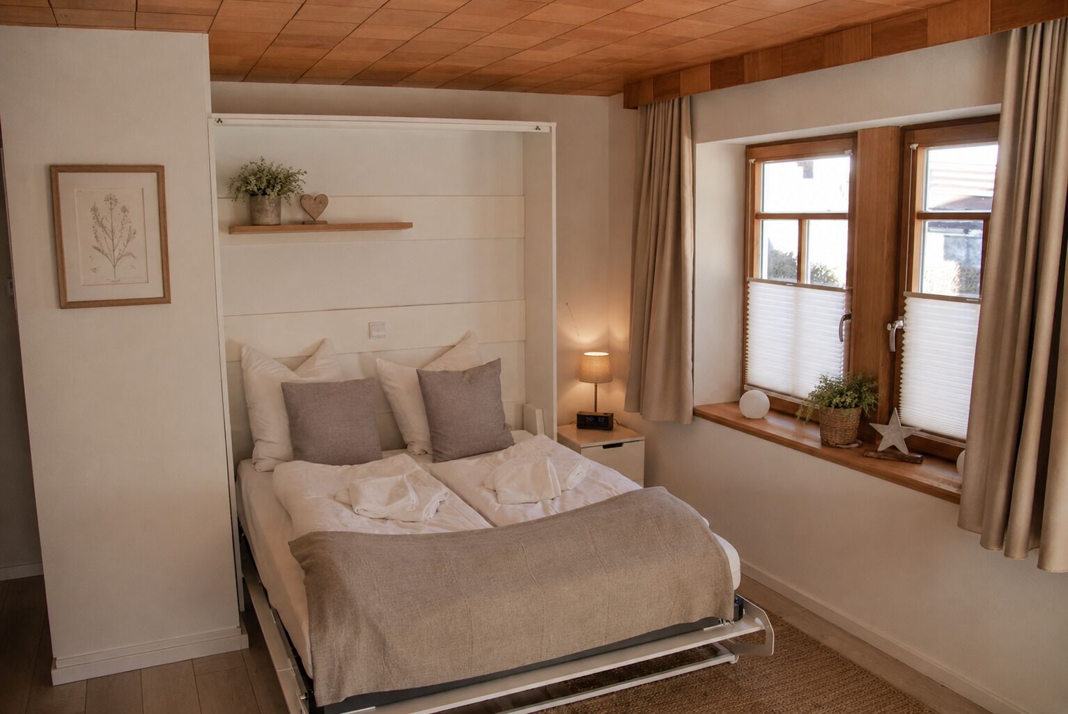 Ein Bett mit Kopfteil, Nachttisch, Lampe und Fenster mit Vorhängen.