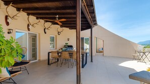 A covered outdoor area with a dining table and chairs, a grill, and antlers on the wall. - Central Marbella Penthouse With Jacuzzi (Marbella)