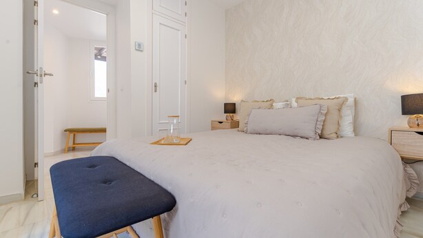 A bedroom with a bed, bedside tables, a bench, and a door leading to another room. - Central Marbella Penthouse With Jacuzzi (Marbella)