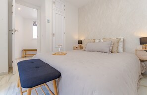 Ein Schlafzimmer mit einem Bett, Nachttischen, einer Bank und einer Tür zu einem anderen Raum.