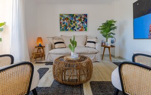 Uma sala de estar com um sofá, uma mesa de centro redonda de vime e duas cadeiras de vime.