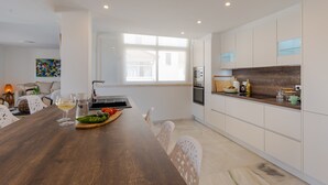 A modern kitchen with white cabinets, a wooden countertop, and a dining area with a dark wooden table and white chairs. - Central Marbella Penthouse With Jacuzzi (Marbella)
