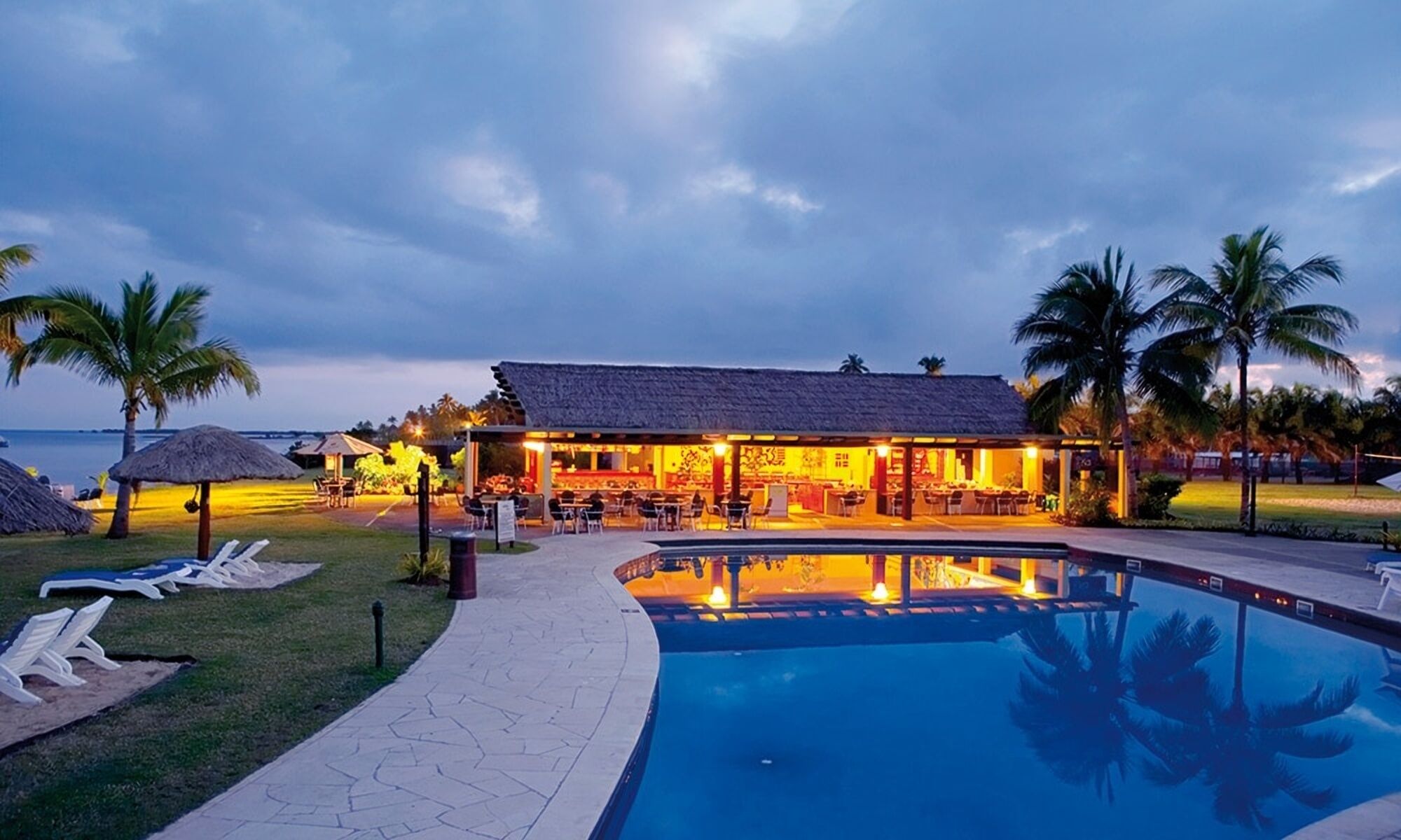 Ett semesterhotell vid stranden med en swimmingpool, solstolar och en bar.