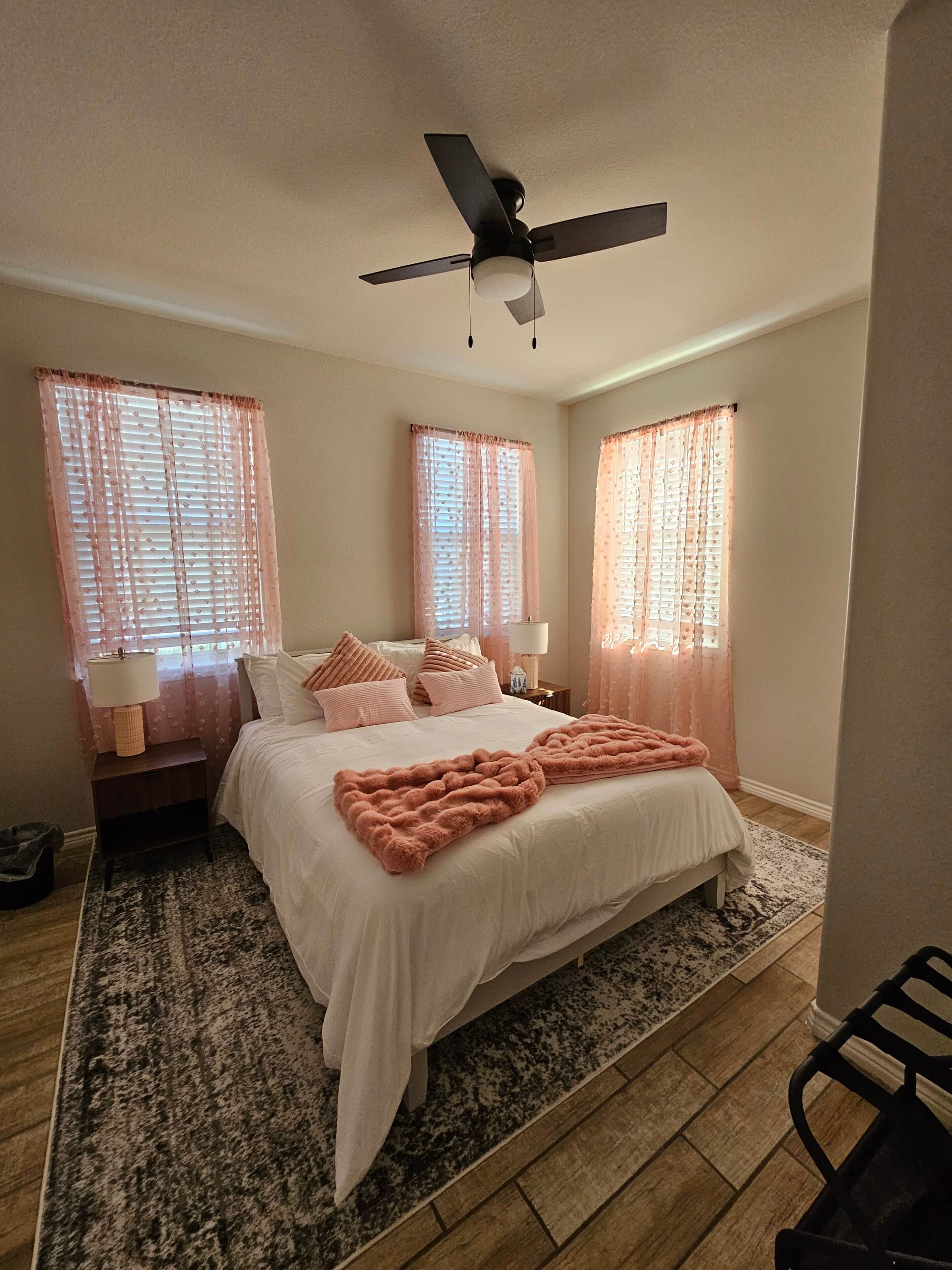 Una camera da letto con un letto, due comodini, una ventola a soffitto e tende rosa.