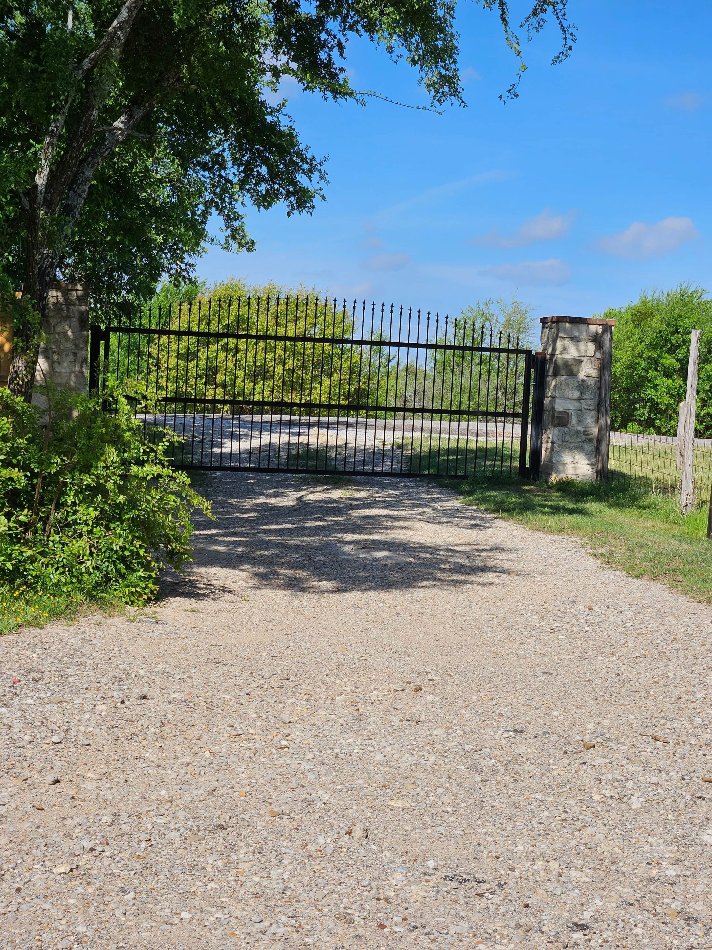 Una strada sterrata che conduce a un cancello chiuso da un pilastro in pietra e un cancello in metallo.
