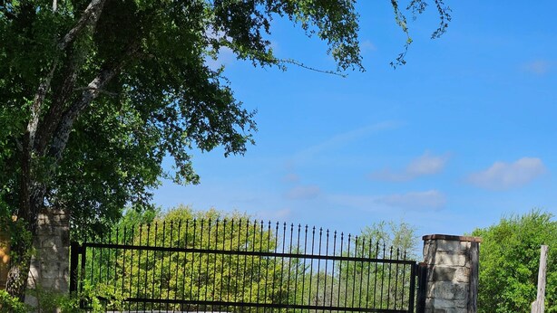 A gravel driveway leading to a gated entrance with a stone pillar and a metal gate.