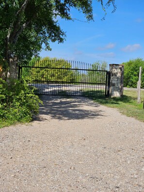 A gravel driveway leading to a gated entrance with a stone pillar and a metal gate.