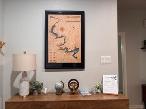 A framed map of Lake Granbury on a wall, a lamp, a globe, a vintage telescope, a small potted plant, a decorative bird, and a welcome sign.