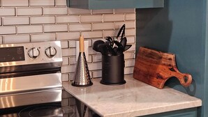 A kitchen with a stainless steel stove, a grater, a utensil holder, and a wooden cutting board on the counter.