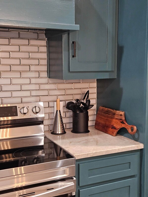 A kitchen with a stainless steel stove, a grater, a utensil holder, and a wooden cutting board on the counter.