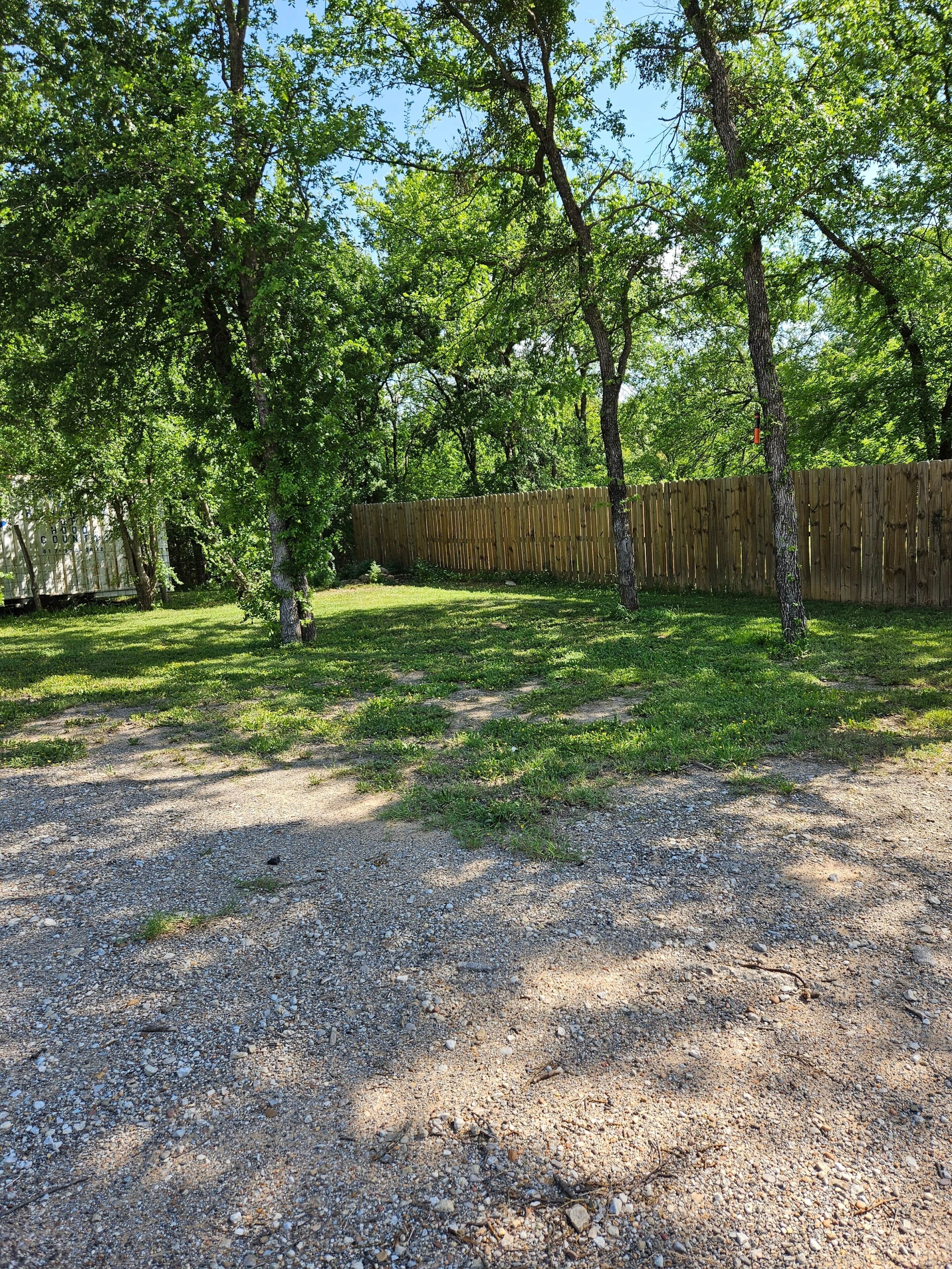 A backyard with a gravel path, trees, and a wooden fence.