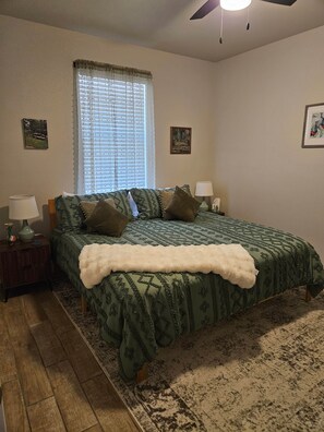 A bedroom with a bed, two bedside tables, a window with blinds, and a ceiling fan.
