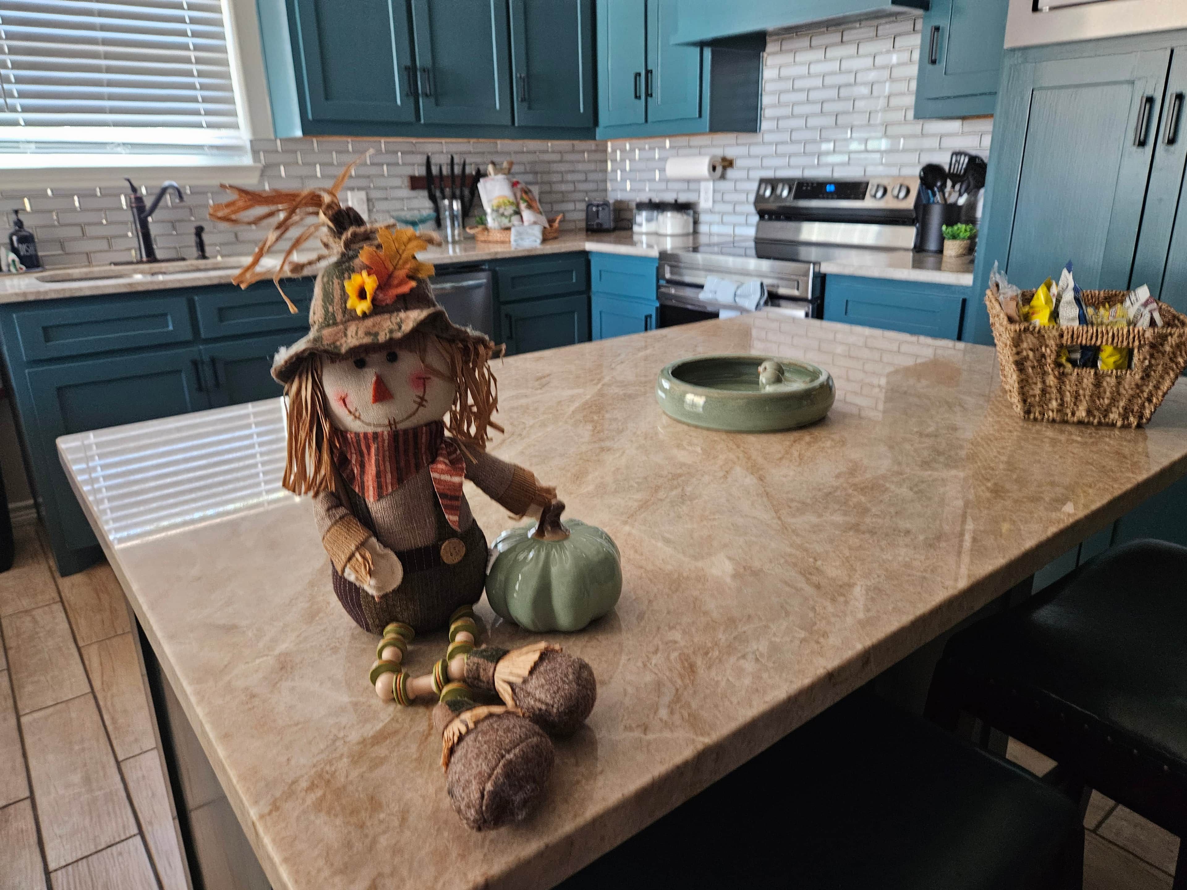 Een keuken met blauwgroene kastjes, een marmeren aanrecht en een decoratieve stroperfiguur.