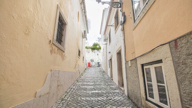 Una estrecha calle adoquinada flanqueada por edificios con ventanas protegidas por rejas y un colgador de luces.