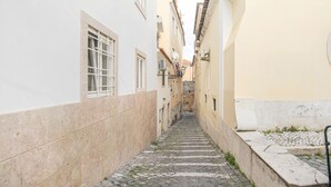 Un estrecho callejón adoquinado entre edificios con fachadas blancas y amarillas, una pared de piedra a un lado y una barandilla de metal al otro.