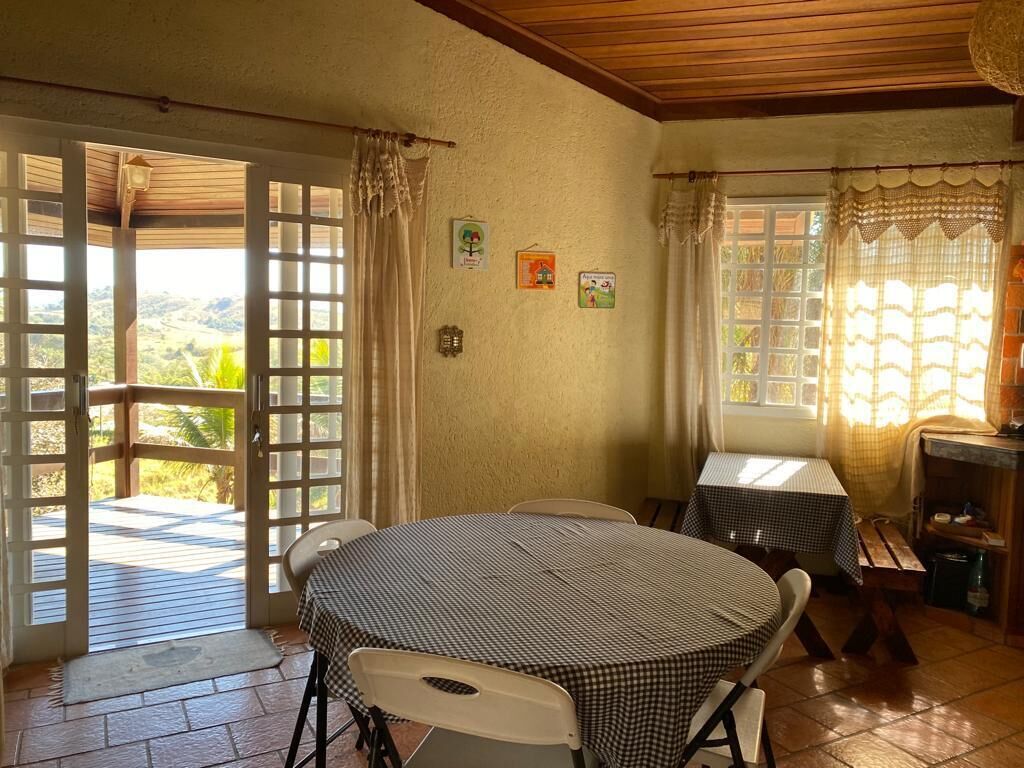 Un comedor con una mesa redonda y sillas, una mesita con mantel a cuadros y vistas al exterior a través de un ventanal de vidrio.