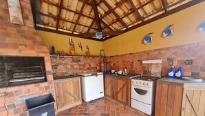 A kitchen with a brick floor, wooden cabinets, a white refrigerator, a stove, and a grill. - Sítio Encanto Brumadinho - Lodging near INHOTIM, ideal for families. (Brumadinho)