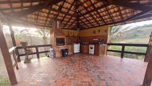 A covered outdoor kitchen area with a brick floor, a grill, and a sink. - Sítio Encanto Brumadinho - Lodging near INHOTIM, ideal for families. (Brumadinho)
