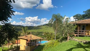 A yellow building with a pool, surrounded by lush greenery and hills. - Sítio Encanto Brumadinho - Lodging near INHOTIM, ideal for families. (Brumadinho)
