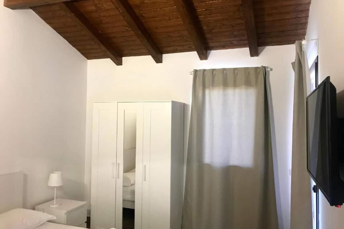 Ein Schlafzimmer mit Holzbalkendecke, einem Kleiderschrank, einem Bett, einem Nachttisch, einem Fernseher und einem Vorhang.