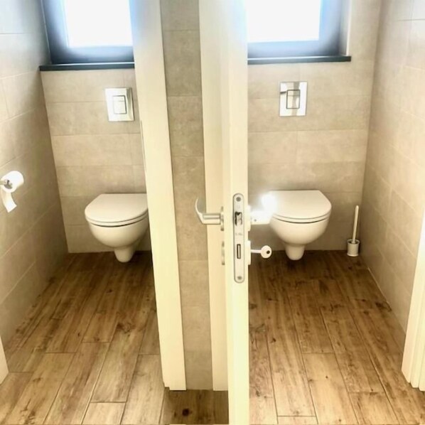 A bathroom with two toilets, a wooden floor, and a window above one toilet. - Agricampeggio Verde Etna (Aci Sant'Antonio)
