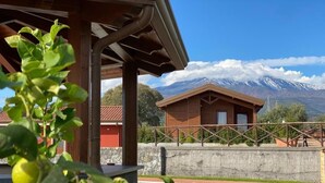 Un chalet en bois avec un mur de pierres et une piscine, situé au pied de montagnes enneigées.