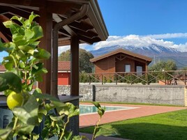 Una cabaña de madera con pared de piedra y piscina, con montañas nevadas al fondo.