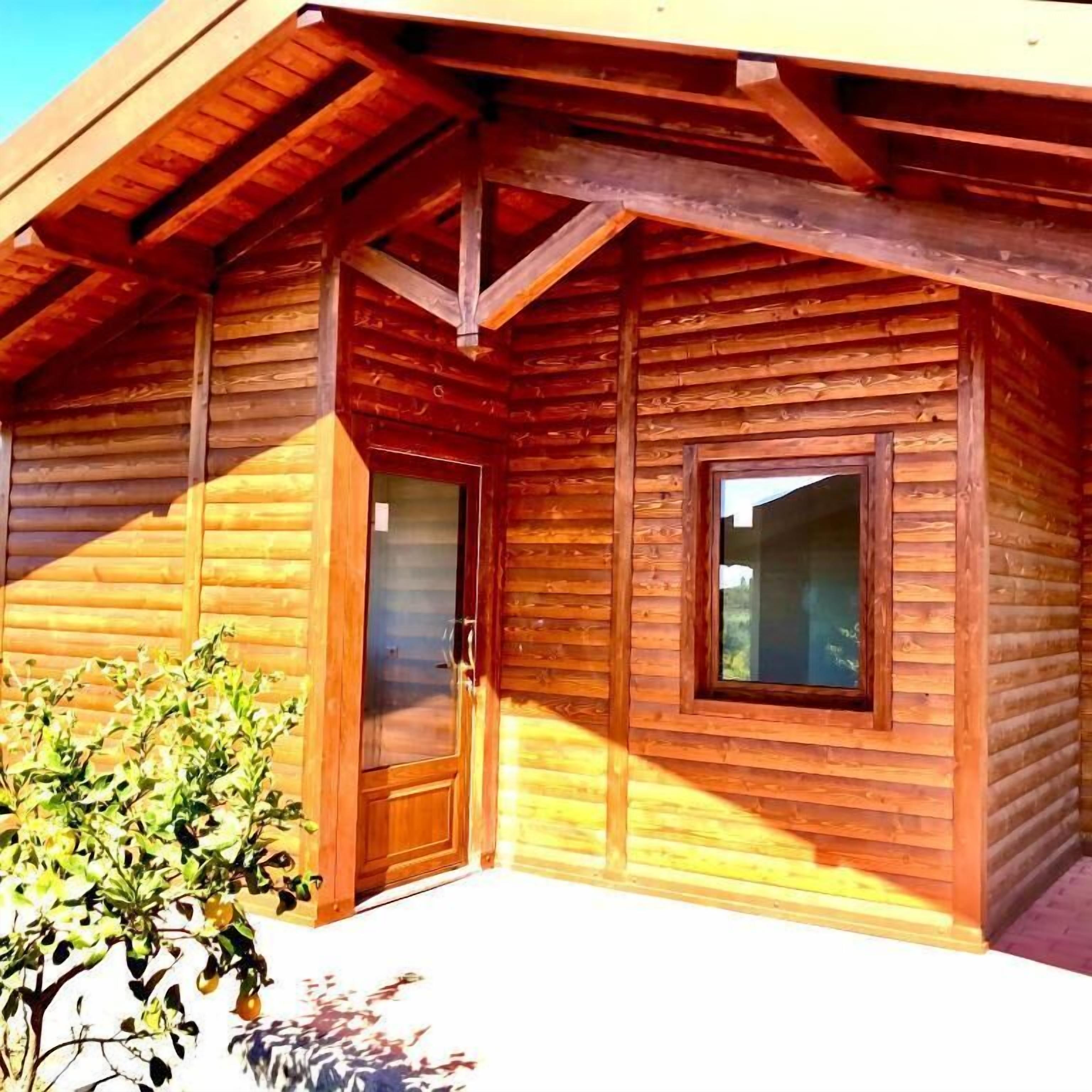 Een houten chalet met een groot raam en een deur, omgeven door een houten terras.