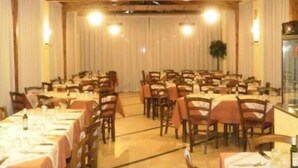 Une grande salle à manger avec des poutres en bois au plafond, des tables recouvertes de nappes blanches et des chaises, ainsi qu’une grande fenêtre ornée de rideaux.