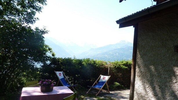 Eine Terrasse mit Tisch und Stühlen, Blick auf Berge und ein Gebäude im Hintergrund.