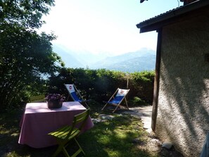 A patio with a table and chairs, a view of mountains, and a building in the background. - Chalet with exceptional view of Mont Blanc! (PASSY)