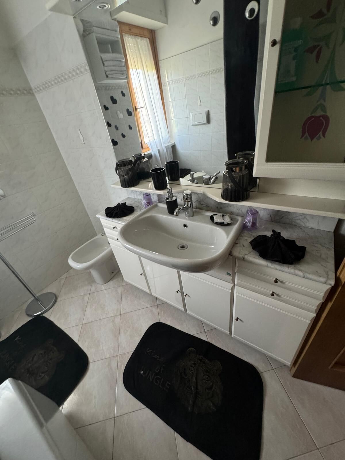 Ein Badezimmer mit Waschbecken, Spiegel und Schränken. Handtuchhalter und Toilette vorhanden.