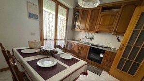 A dining area with a table set for four, wooden cabinets, a stove, and a window with curtains. - The house of mihaela 10 minutes from the private beach le Dune di Forte dei marmi (Capanne-Prato-Cinquale)