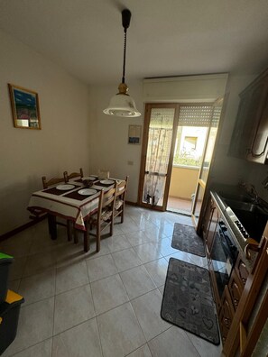 A dining area with a table and chairs, a ceiling fan, a kitchen with a stove and sink, and a sliding glass door leading to a balcony. - The house of mihaela 10 minutes from the private beach le Dune di Forte dei marmi (Capanne-Prato-Cinquale)