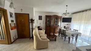A living room with a beige sofa, wooden cabinet, and dining area with a table and chairs. - The house of mihaela 10 minutes from the private beach le Dune di Forte dei marmi (Capanne-Prato-Cinquale)