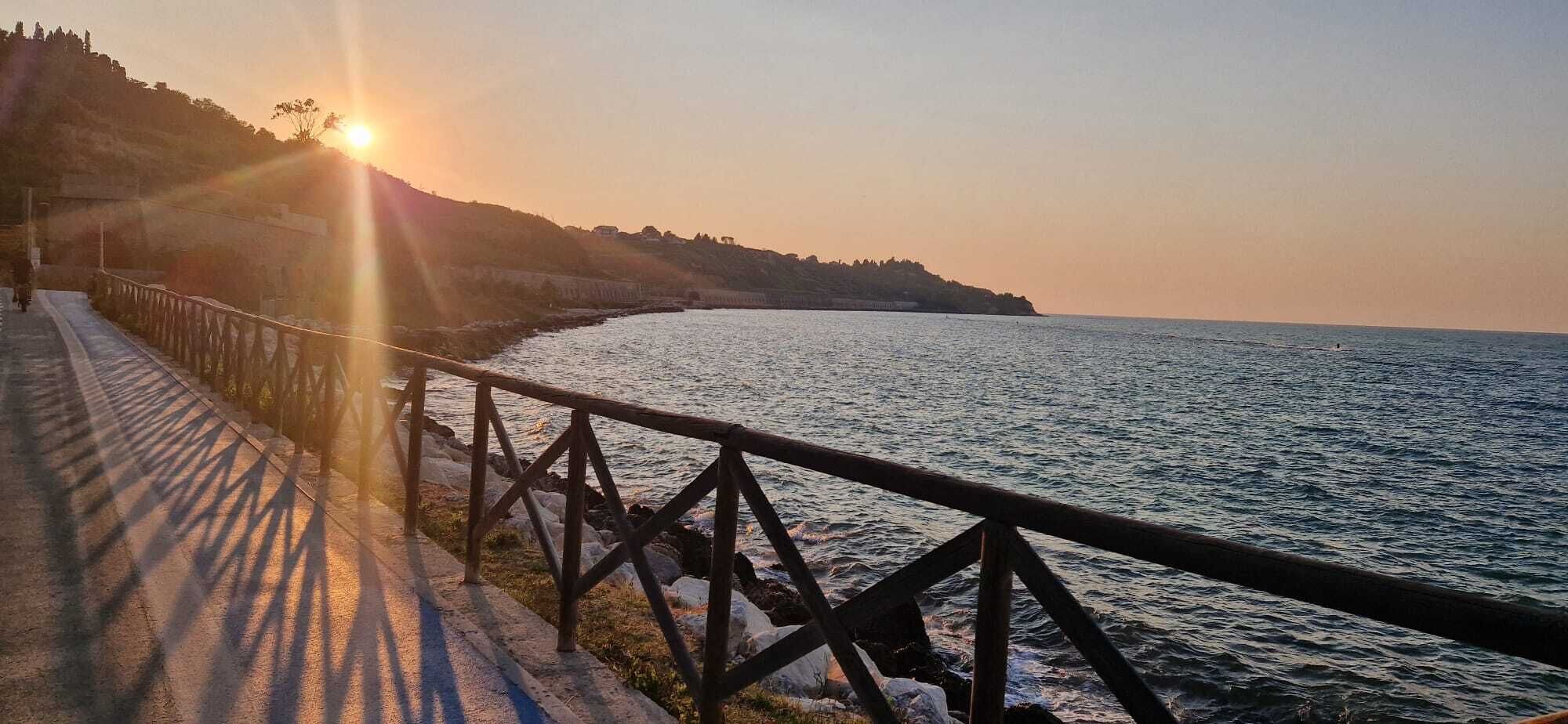 A coastal walkway with a metal railing, leading to the sea, during sunset.