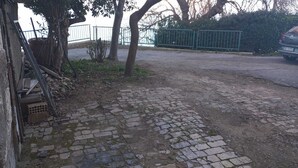 Een geplaveid gebied met een combinatie van straatklinkers en aarde, omgeven door bomen en een metalen hek.