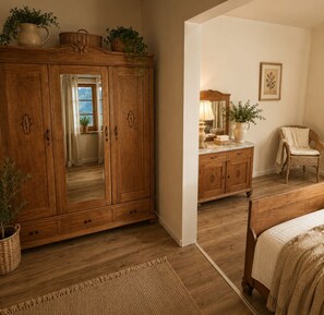 A room with a wooden wardrobe, a bed, a wicker chair, and a mirror. - Landhaus am See - Apartment Lärenberg, directly on Lake Edersee (Waldeck)