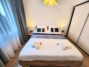 A hotel room with a bed, two bedside lamps, a nightstand, and a large window with curtains. - Cosy House With Swimming Pool - Bergerac (5 minutes from downtown) (Bergerac)