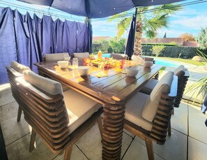 An outdoor dining area with a wooden table, cushioned chairs, and a fire feature. - Cosy House With Swimming Pool - Bergerac (5 minutes from downtown) (Bergerac)
