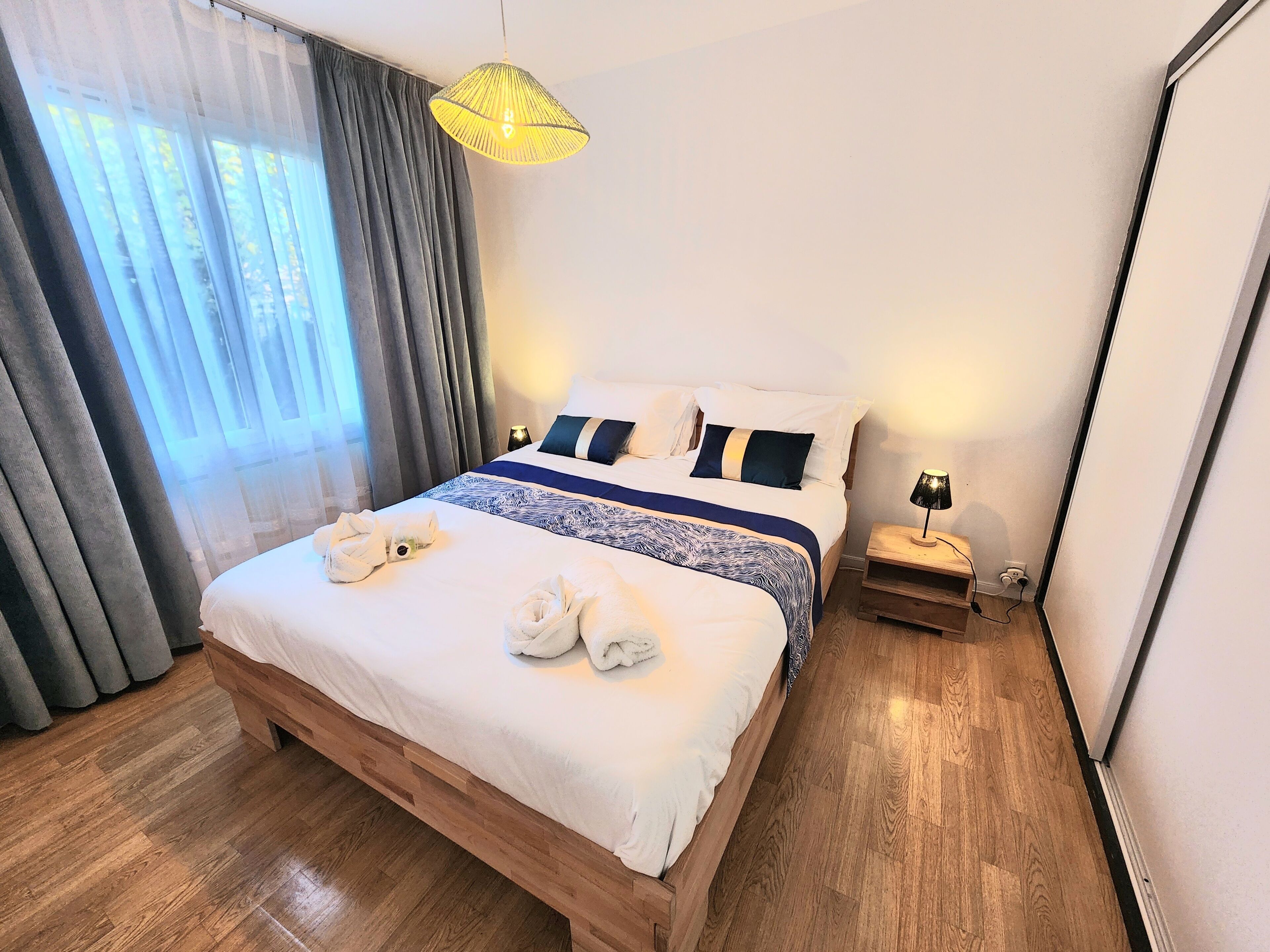 Une chambre d’hôtel avec un lit en bois, une lampe de chevet et une fenêtre avec des rideaux.