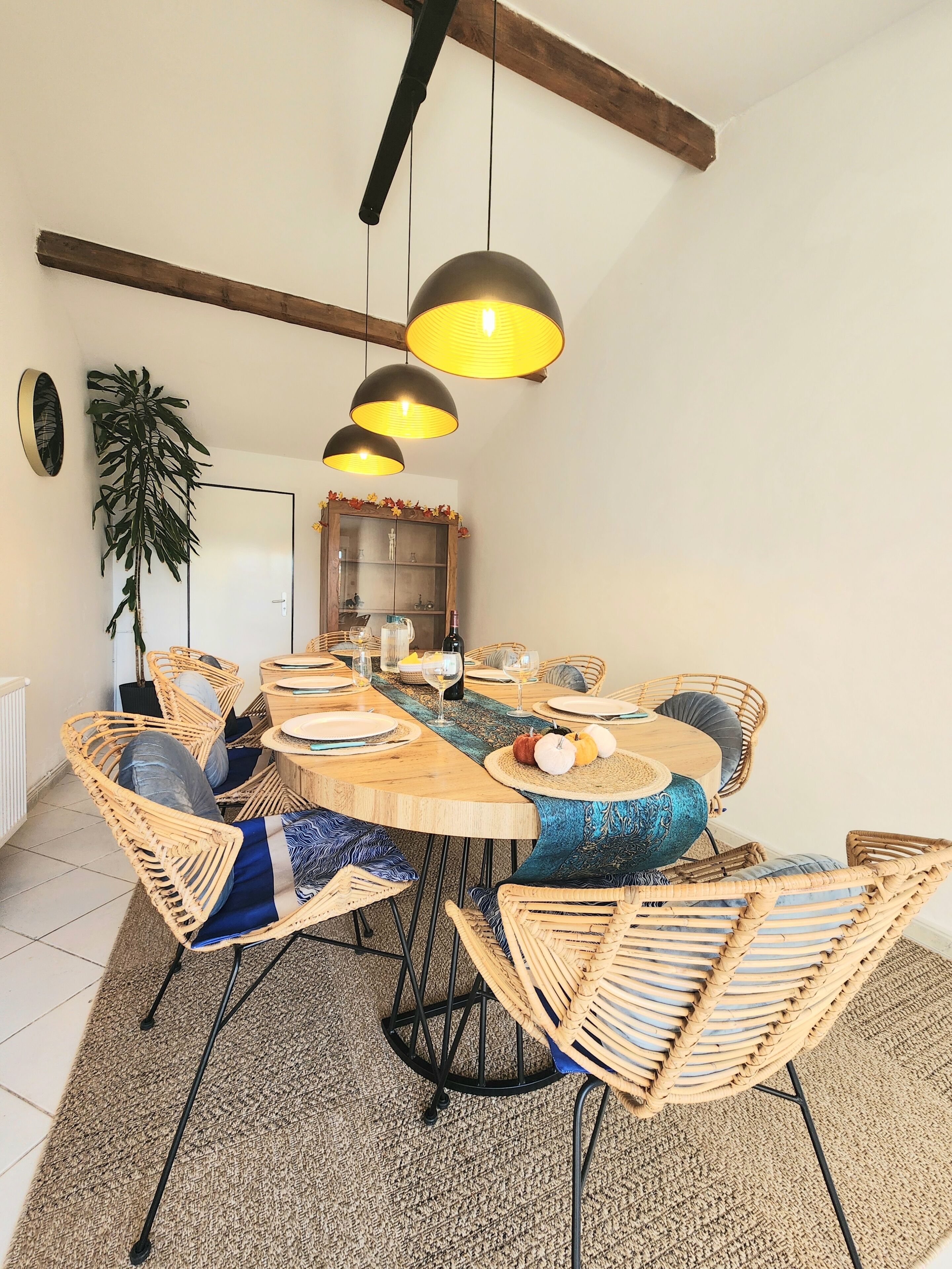 Een eetgedeelte met een ronde tafel, rieten stoelen en hanglampen.