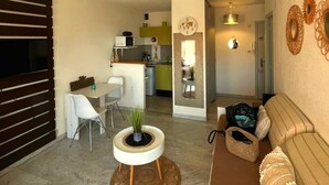 A compact living space with a dining area, kitchenette, and a sofa with decorative pillows. - Apartment in cosy residence with magnificent view of the port (Occitanie)