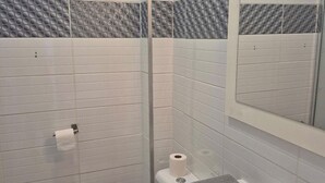 A modern bathroom with white subway tiles, a glass shower enclosure, a toilet, a sink with a towel, and a mirror. - Apartment in cosy residence with magnificent view of the port (Occitanie)