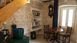 A rustic kitchen with a stone wall, wooden staircase, and a dining area with a round table and chairs. - Golubica: A Romantic 17th Century Stone UNESCO Retreat (Stari Grad)