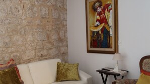 A living room with a stone wall, a white sofa, a wooden coffee table, a patterned rug, and a framed painting. - Golubica: A Romantic 17th Century Stone UNESCO Retreat (Stari Grad)
