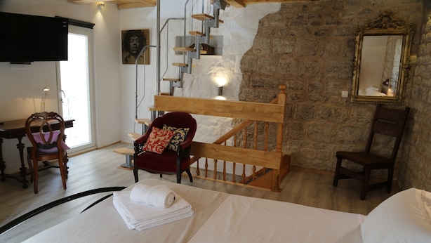 A hotel room with a wooden bed, a red armchair, a wooden chair, a staircase, and a stone wall. - Golubica: A Romantic 17th Century Stone UNESCO Retreat (Stari Grad)