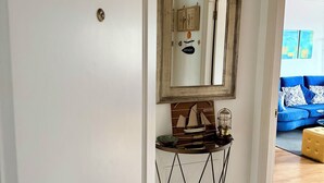 A hallway with a white door, a console table with a ship model, a mirror, and a blue sofa in the background.