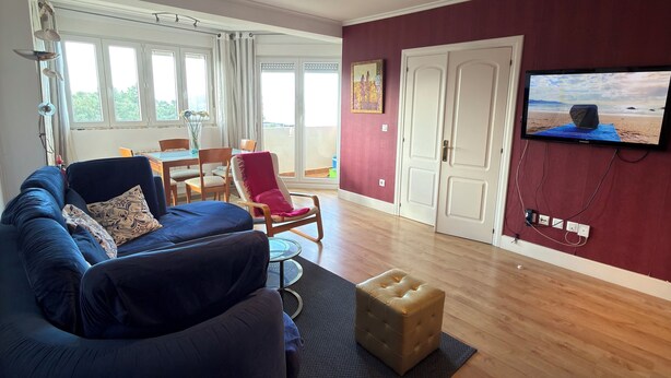 A modern living room with a blue sofa, a red chair, a wooden coffee table, and a television mounted on the wall.