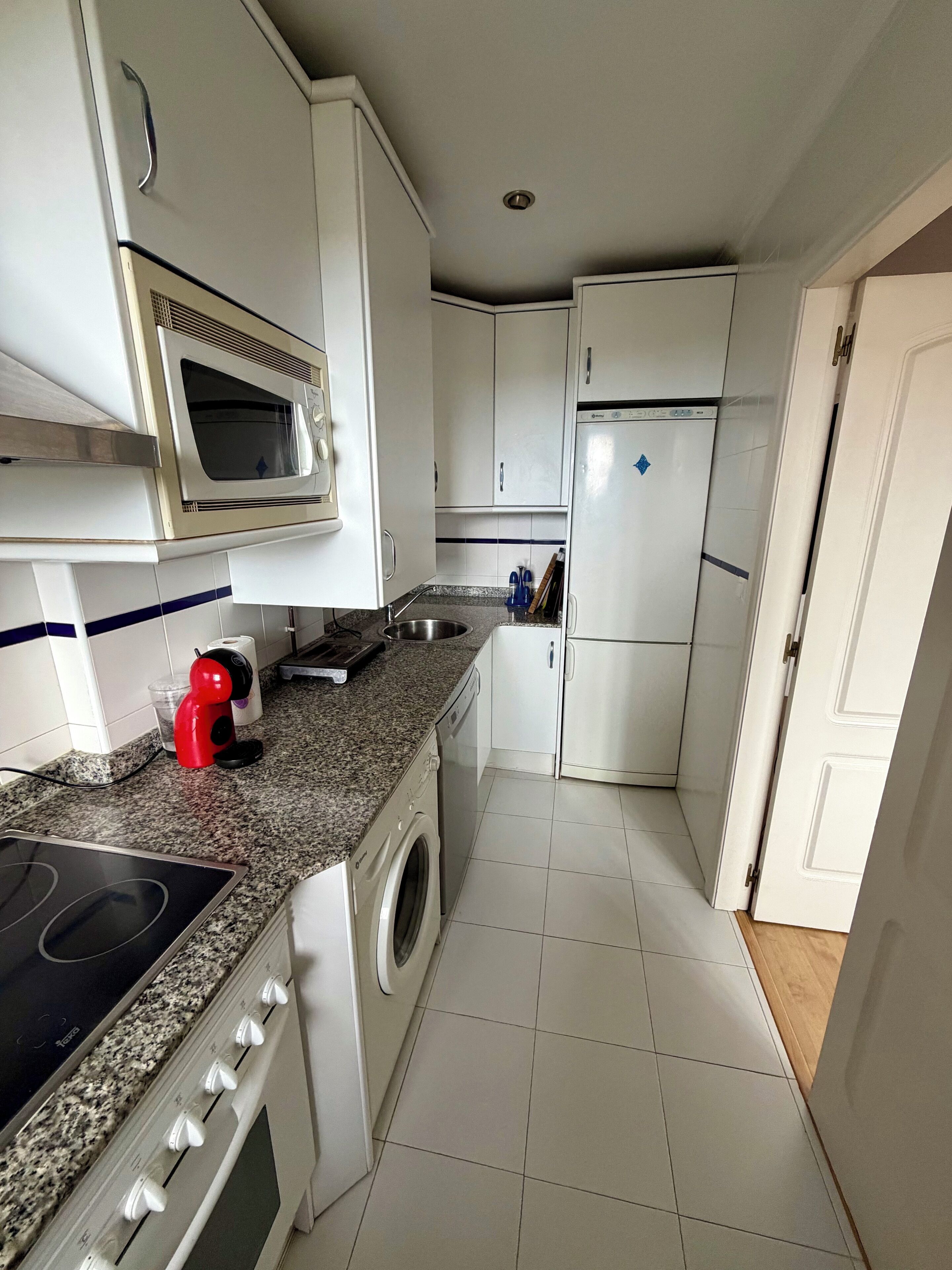 A compact kitchen with white cabinets, a microwave, a dishwasher, a stove, and a washing machine.